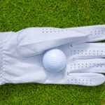 high-angle-closeup-golf-ball-glove-lawn-sunlight-min